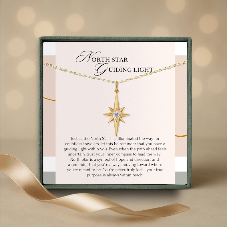 K&ouml;nnte beinhalten: Eine goldfarbene Halskette mit einem Nordstern-Anh&auml;nger, pr&auml;sentiert in einer Geschenkbox. Der Anh&auml;nger hat ein Sternenmuster mit einem zentralen Edelstein. Die Box tr&auml;gt den Text "North Star Guiding Light" und eine Botschaft &uuml;ber Hoffnung.