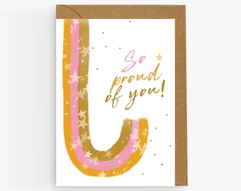 May include: A white card with a pink and gold rainbow design and the text "So proud of you!" in gold lettering. The card has a brown envelope.