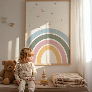 Könnte beinhalten: Ein Kind sitzt auf einer Bank unter einem gerahmten Regenbogen-Kunstdruck. Ein Teddybär, ein Holzspielzeug zum Stapeln und eine gefaltete Decke befinden sich ebenfalls auf der Bank. Das Kind trägt einen floral bedruckten Anzug.
