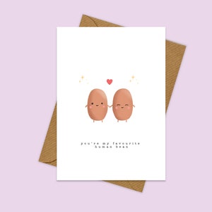 May include: A white card with two brown cartoon beans holding hands. The beans have happy faces and there is a red heart above them. The text on the card reads "You're my favourite human bean."