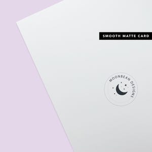 May include: A white card with the text "SMOOTH MATTE CARD" printed in black at the top. A circular logo with the text "MOONBEAN DESIGNS" and a crescent moon with stars is printed in the bottom right corner.
