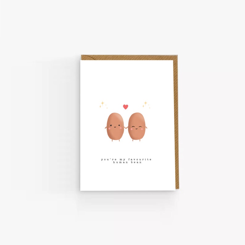 May include: A white card with two brown beans holding hands and a red heart above them. The text on the card reads "you're my favourite human bean."
