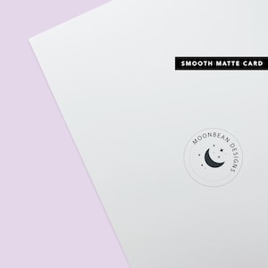 May include: A white card with the text "SMOOTH MATTE CARD" printed in black at the top. A circular logo with the text "MOONBEAN DESIGNS" and a crescent moon with stars is printed in the bottom right corner.