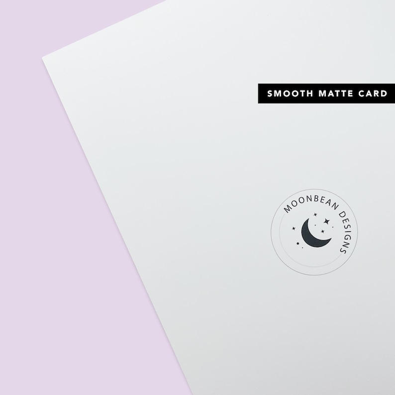 May include: A white card with the text "SMOOTH MATTE CARD" printed in black at the top. A circular logo with the text "MOONBEAN DESIGNS" and a crescent moon with stars is printed in the bottom right corner.