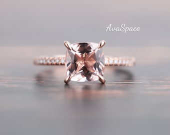May include: A rose gold engagement ring with a large, square-cut, light pink gemstone surrounded by a band of smaller diamonds.