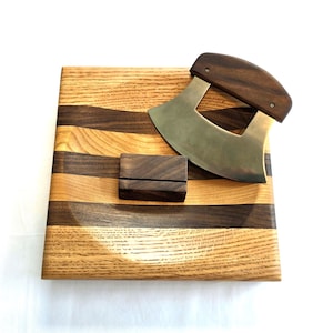 Peut inclure: Une planche &agrave; d&eacute;couper en bois avec un motif ondul&eacute; en noyer et en ch&ecirc;ne. La planche est dot&eacute;e d'un petit support en bois et d'un couteau incurv&eacute; en acier inoxydable avec un manche en bois.