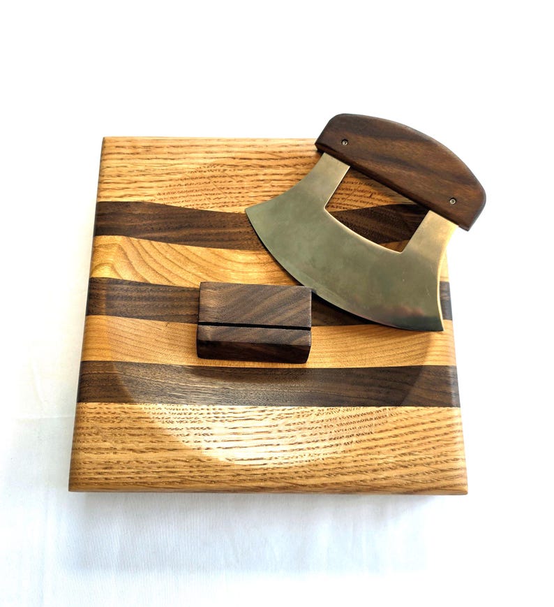 Peut inclure: Une planche &agrave; d&eacute;couper en bois avec un motif ondul&eacute; en noyer et en ch&ecirc;ne. La planche est dot&eacute;e d'un petit support en bois et d'un couteau incurv&eacute; en acier inoxydable avec un manche en bois.