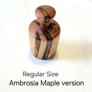 May include: A wooden Ambrosia Maple version of a regular size object. The object is cylindrical with a rounded top. The wood grain features dark brown streaks and knots. The text "Regular Size Ambrosia Maple version" is below the object.