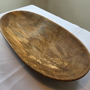 May include: Oval wooden bowl with a natural wood grain finish. The bowl is a light brown color with darker brown and tan accents. The bowl is approximately 18 inches long and 8 inches wide, perfect for serving or display.