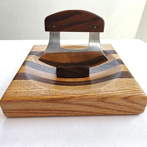 Peut inclure: Une planche &agrave; d&eacute;couper en bois avec une zone creus&eacute;e incurv&eacute;e pour un couteau. La planche est en bois de ch&ecirc;ne et de noyer et a une finition brun fonc&eacute;. Un couteau en acier inoxydable avec un manche en bois repose dans la zone creus&eacute;e.