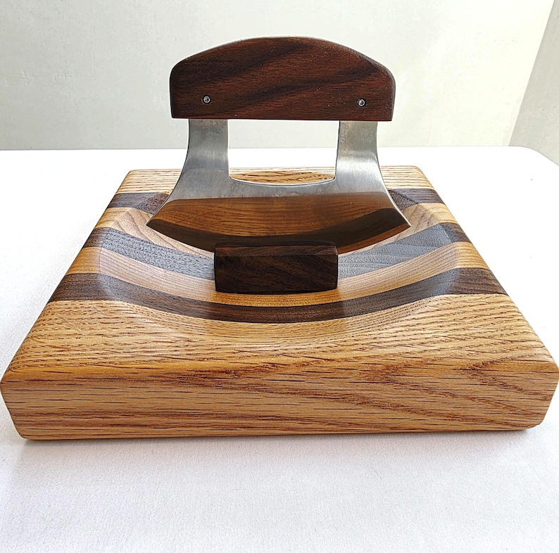 Peut inclure: Une planche &agrave; d&eacute;couper en bois avec une zone creus&eacute;e incurv&eacute;e pour un couteau. La planche est en bois de ch&ecirc;ne et de noyer et a une finition brun fonc&eacute;. Un couteau en acier inoxydable avec un manche en bois repose dans la zone creus&eacute;e.