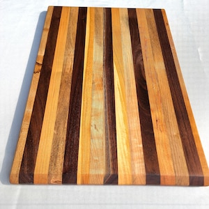 Peut inclure: Une grande planche à découper en bois avec un motif rayé de bois clair et foncé. La planche est faite de plusieurs types de bois, dont le noyer et l'érable.