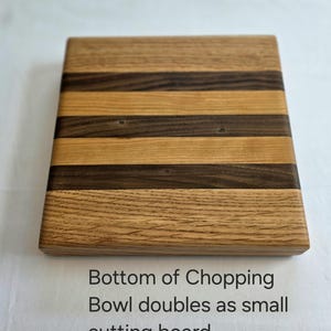 Peut inclure: Une planche &agrave; d&eacute;couper en bois avec un motif ray&eacute; de bois clair et fonc&eacute;. Le dessous de la planche est visible sur l'image. Le texte "Bottom of Chopping Bowl doubles as small cutting board." est imprim&eacute; sous la planche.