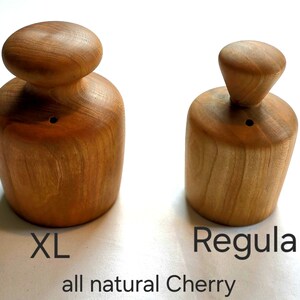 May include: Two wooden kitchen tools, one labeled "XL" and the other "Regular". Both are made of natural cherry wood. The XL tool has a rounded top, while the Regular tool has a conical top. The text "all natural Cherry" is below.