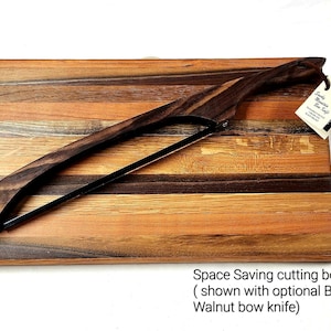 Op de afbeelding: Ruimtebesparend snijplank van hout met een uniek houtnerfpatroon. De plank wordt getoond met een optioneel zwart walnoot-boogmes. Het mes heeft een houten handvat en een zwarte kling.