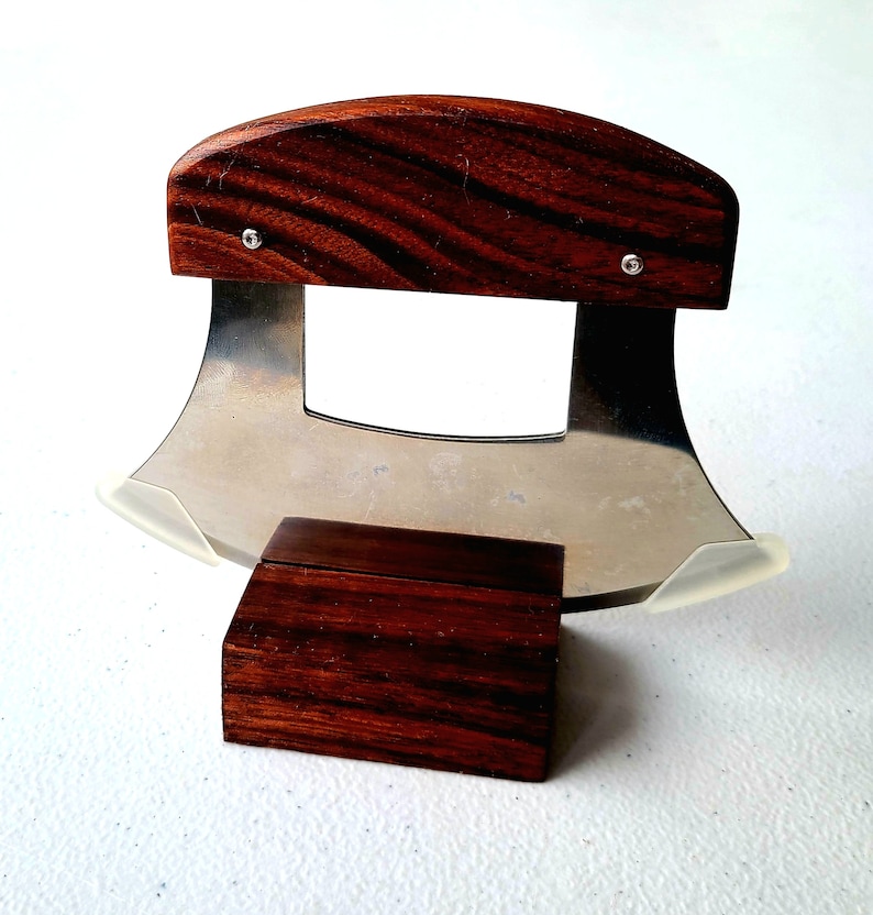 Peut inclure: Un couteau &agrave; lame courbe en acier inoxydable avec un manche en bois et un support en bois. Le couteau a une garde en plastique transparent sur la lame.