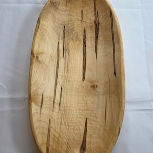 May include: Oval wooden bowl with a natural finish. The bowl has a light brown color with dark brown streaks and knots. The interior is smooth and the edges are rounded. A decorative piece for the home.