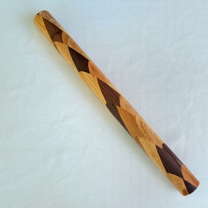 May include: A wooden rolling pin with a unique design featuring alternating sections of light and dark wood. The wood is arranged in a chevron pattern, creating a visually appealing and textured surface.