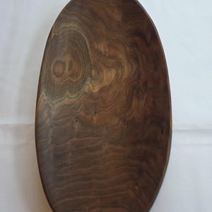 May include: Oval-shaped wooden bowl with a dark brown finish. The bowl has a smooth, polished surface with visible wood grain patterns. The edges are slightly curved, and the bowl appears to be empty. The wood has a natural, organic look.