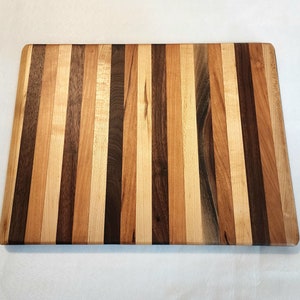 May include: A rectangular wooden cutting board with a striped pattern of light and dark wood. The board is made of multiple wood types, including maple, walnut, and cherry.
