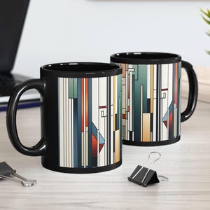 May include: Two black ceramic coffee mugs with a geometric design of vertical lines in shades of red, blue, beige, and green. The mugs have a black handle and interior. The mugs are on a light-colored surface.