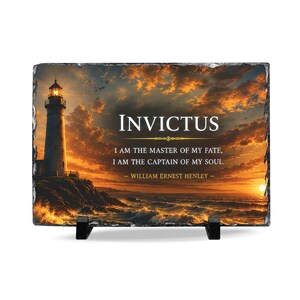 May include: A rectangular slate plaque featuring a lighthouse on a rocky cliff at sunset. The text reads: INVICTUS, I AM THE MASTER OF MY FATE, I AM THE CAPTAIN OF MY SOUL. — WILLIAM ERNEST HENLEY. The plaque is supported by two black stands.