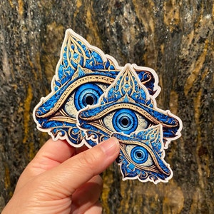 May include: Three blue and gold eye stickers with intricate designs. The eyes are surrounded by ornate patterns and have a mystical feel.