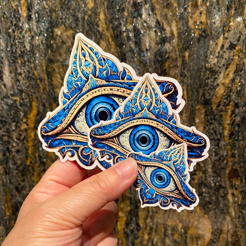 May include: Three blue and gold eye stickers with intricate designs. The eyes are surrounded by ornate patterns and have a mystical feel.