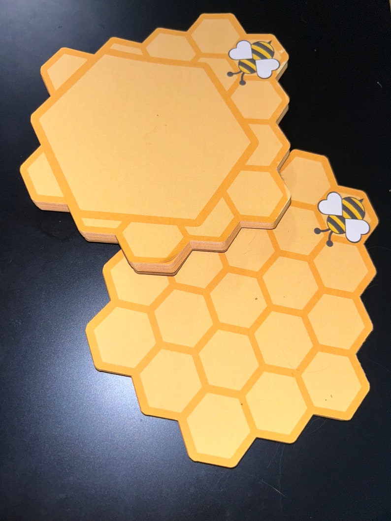 Puede incluir: Un conjunto de posavasos amarillos en forma de panal con un gr&aacute;fico de abeja de dibujos animados. Los posavasos tienen un centro amarillo claro con un borde amarillo m&aacute;s oscuro. El gr&aacute;fico de la abeja es negro y amarillo con alas blancas.