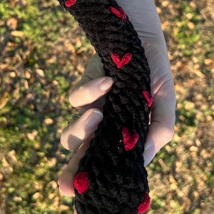 Op de afbeelding: Zwart touw met rode fluwelen harten erop genaaid. Het touw is dik en heeft een zachte textuur.