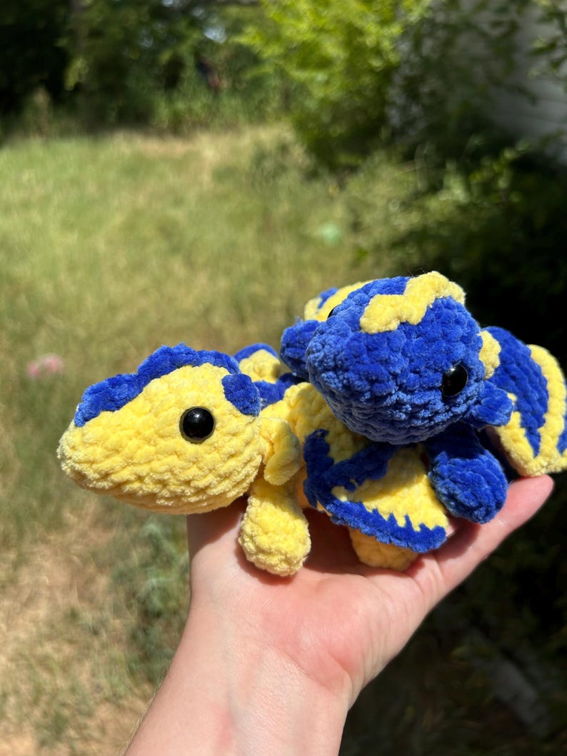 Puede incluir: Dos peque&ntilde;os peluches de ganchillo hechos a mano con una textura suave y difusa. Un peluche es principalmente amarillo con manchas azules, y el otro es principalmente azul con manchas amarillas. Ambos tienen ojos redondos negros y alas.