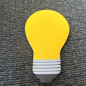 May include: A yellow lightbulb-shaped sticky note with a black and white striped base.