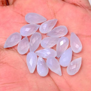 Puede incluir: Una colecci&oacute;n de gemas en forma de l&aacute;grima de color lavanda p&aacute;lido con superficies facetadas. Las gemas est&aacute;n dispuestas sobre una superficie rosa claro, mostrando su cualidad transl&uacute;cida y sutiles variaciones de color. Ideales para la creaci&oacute;n de joyas.
