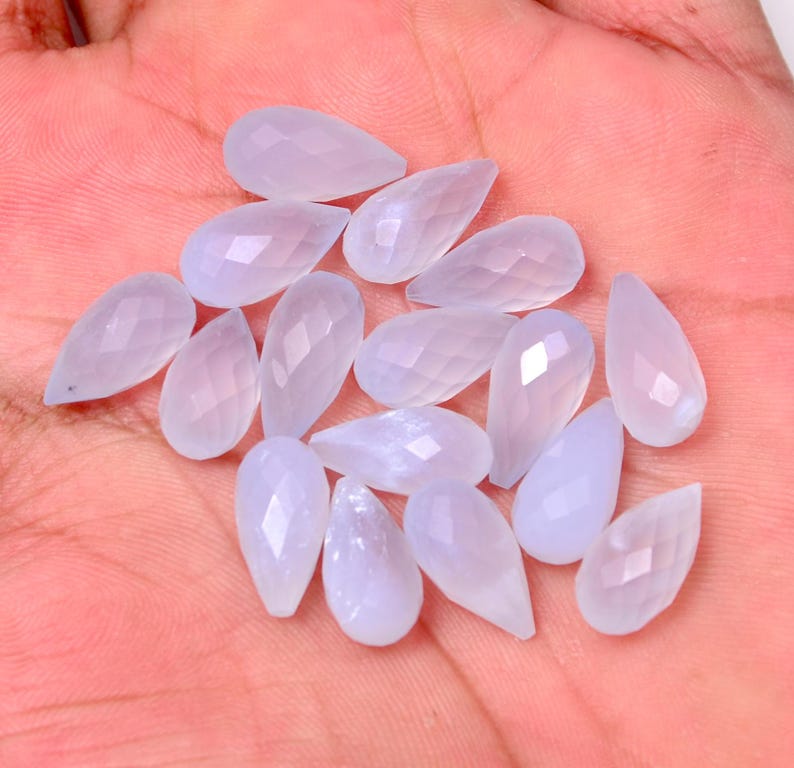 Puede incluir: Una colecci&oacute;n de gemas en forma de l&aacute;grima de color lavanda p&aacute;lido con superficies facetadas. Las gemas est&aacute;n dispuestas sobre una superficie rosa claro, mostrando su cualidad transl&uacute;cida y sutiles variaciones de color. Ideales para la creaci&oacute;n de joyas.