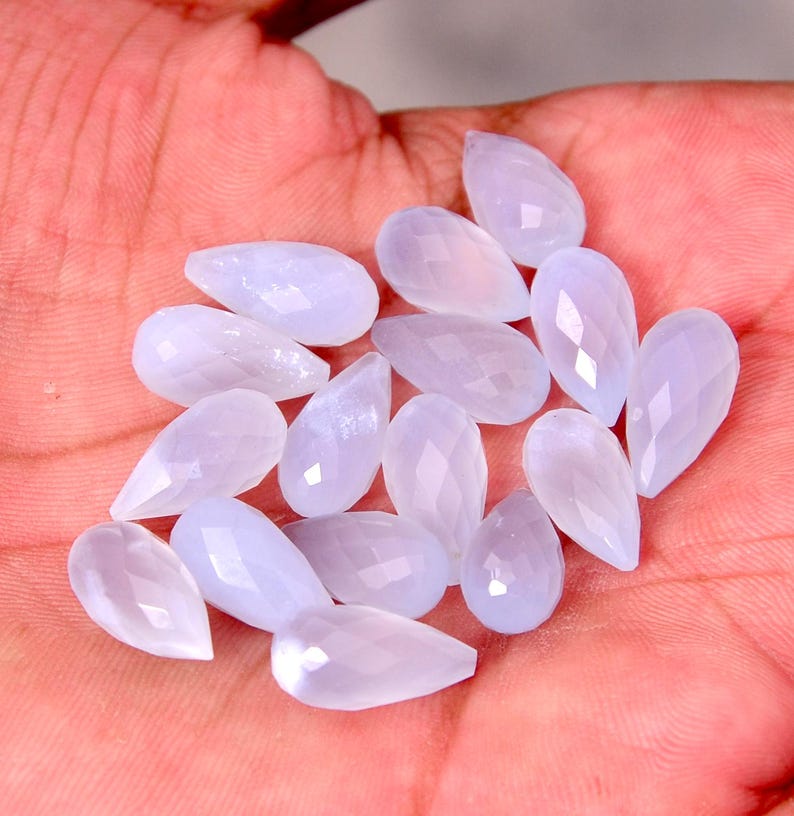 Puede incluir: Un conjunto de gemas en forma de l&aacute;grima, de color azul claro, con superficies facetadas. Las gemas se muestran sobre un fondo color piel, resaltando su cualidad transl&uacute;cida y sutiles variaciones de color. Adecuado para la creaci&oacute;n de joyas.