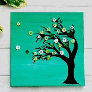May include: A teal canvas painting of a black silhouette of a tree with green, white and yellow buttons attached to the branches.