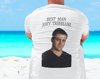 May include: A white t-shirt with the text "BEST MAN JOEY TRIBBIANI" and a photo of Joey Tribbiani. The person wearing the shirt is sitting on a sandy beach with the ocean in the background. The sky is blue.
