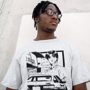 Puede incluir: Una camiseta gris con un estampado gráfico en blanco y negro de un coche, un conductor y el texto "13-600".