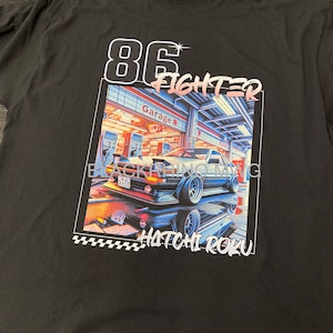 Könnte beinhalten: Schwarzes T-Shirt mit einem Grafikdruck eines weißen Autos mit dem Text "86 Fighter" und "Hachi Roku". Das Auto steht vor einem Gebäude mit Neonlichtern und dem Text "Garage" in japanischer Schrift.