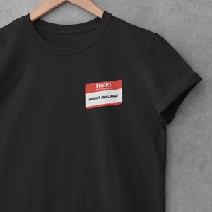 Puede incluir: Camiseta negra con una etiqueta de nombre roja que dice "Hello my name is REGINA PHALANGE"