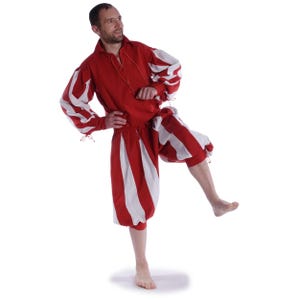 Könnte beinhalten: Ein rot-weiß gestreiftes Renaissance-Kostüm. Das Outfit umfasst ein langärmliges Hemd mit weiß gestreiften Ärmeln und eine passende knielange Hose. Das Hemd hat einen geschnürten Ausschnitt.