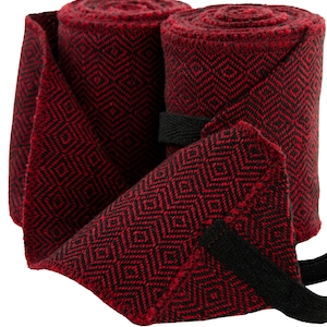 Könnte beinhalten: Zwei gerollte rot-schwarze Stoffwickel mit Rautenmuster. Die Wickel sind mit einem schwarzen Riemen befestigt. Der Stoff ist tiefrot mit einem schwarzen Rautenmuster.