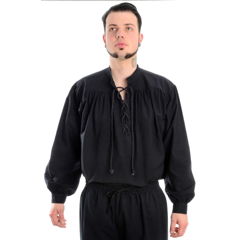 Pode incluir: Camisa preta de manga comprida com decote com atacadores e mangas franzidas. A camisa &eacute; combinada com cal&ccedil;as pretas a condizer. O traje tem um estilo medieval ou renascentista, adequado para reconstitui&ccedil;&otilde;es hist&oacute;ricas ou eventos tem&aacute;ticos.