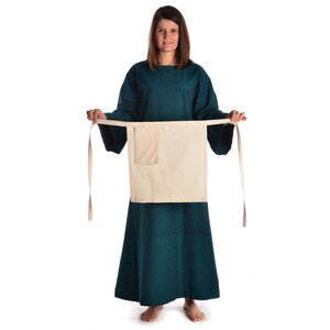 May include: A teal tunic with long sleeves and a white apron with a pocket. The apron is tied at the waist with long ties.