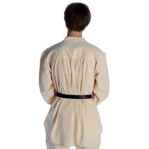 Pode incluir: Uma camisa creme de manga comprida com um cinto preto. A camisa tem gola mandarim e pregas nas costas. O cinto &eacute; feito de couro preto. A camisa &eacute; feita de um tecido leve e respir&aacute;vel.