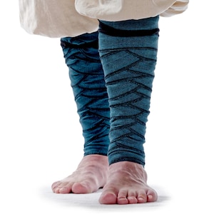 May include: Teal leggings with a black geometric pattern. The leggings are worn on bare feet. The fabric appears to be a textured knit. The leggings are pulled up to the mid-calf.