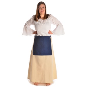 May include: A woman wearing a white peasant blouse with long sleeves and a gathered neckline. She is wearing a cream-colored skirt with a dark blue apron over it.