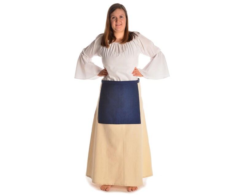 May include: A woman wearing a white peasant blouse with long sleeves and a gathered neckline. She is wearing a cream-colored skirt with a dark blue apron over it.