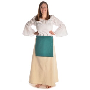 May include: A woman wearing a white peasant blouse with a green apron over a long beige skirt.