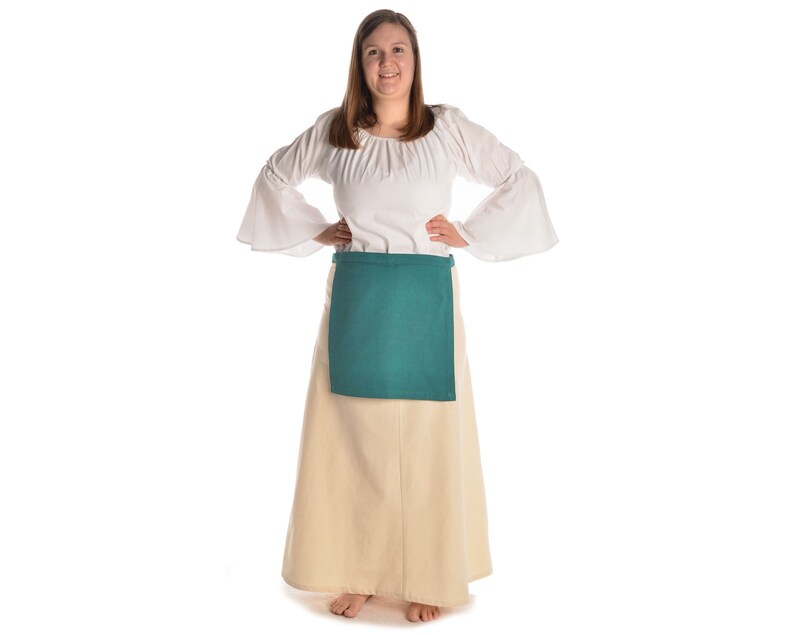 May include: A woman wearing a white peasant blouse with a green apron over a long beige skirt.